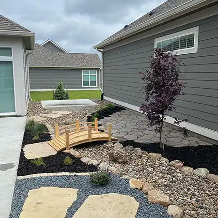 The space between a house and garage is decorated with stone walkways and rockwork 