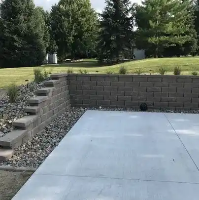 A stone wall and garden bed sits near a large, open green space