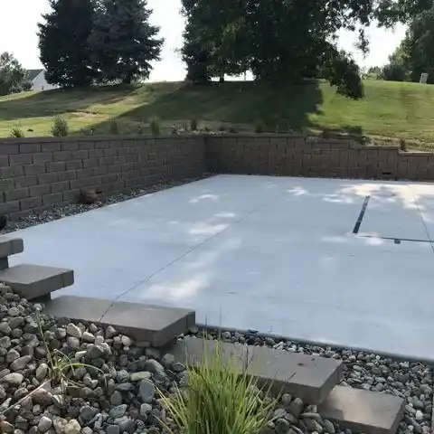 A stone wall and garden bed surround a concrete sport court area