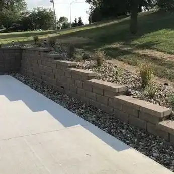 A stone wall and garden bed surround a concrete sport court area