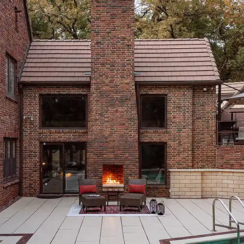 An outdoor patio area with a fireplace and two chairs that are set near a pool