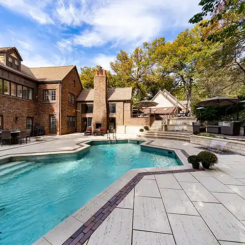 An outdoor living space with multiple seating areas, shade umbrellas, a stone staircase, and a pool
