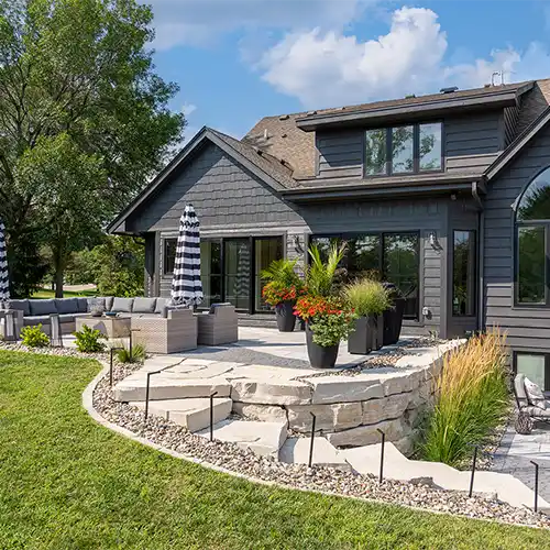 An outdoor living space features couches, chairs, a table, umbrellas, and a stone staircase