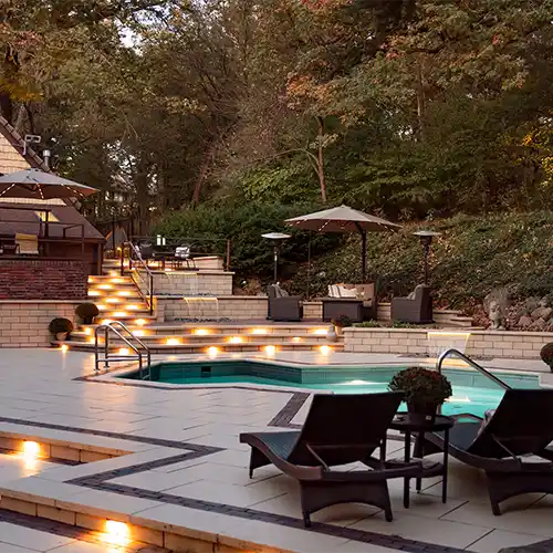 An outdoor living space with multiple seating areas, shade umbrellas, a stone staircase, and a pool