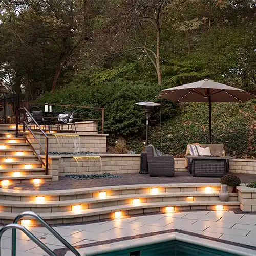 A multi-level outdoor living space with a stone staircase, seating areas, a pool, and a fountain