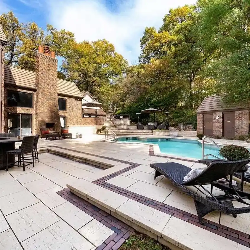 An outdoor pool sits next to an outdoor living space with shaded seating, fireplace, and fountains