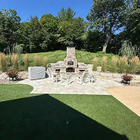 A turf area sits next to a stone patio with seating and a fireplace