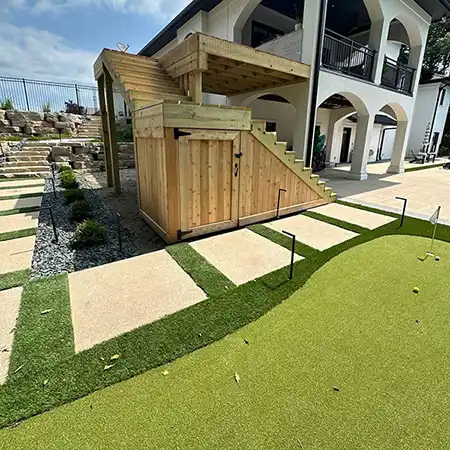 A turf putting green sits beside a stone walkway 